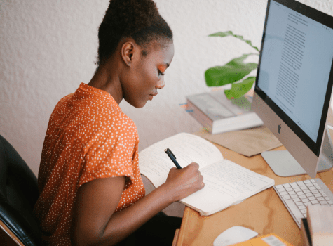 Jeune femme qui prend des notes papiers depuis son ordinateur